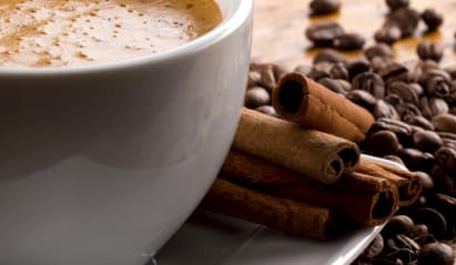 Coffee cup with cinnamon sticks and coffee beans on the table