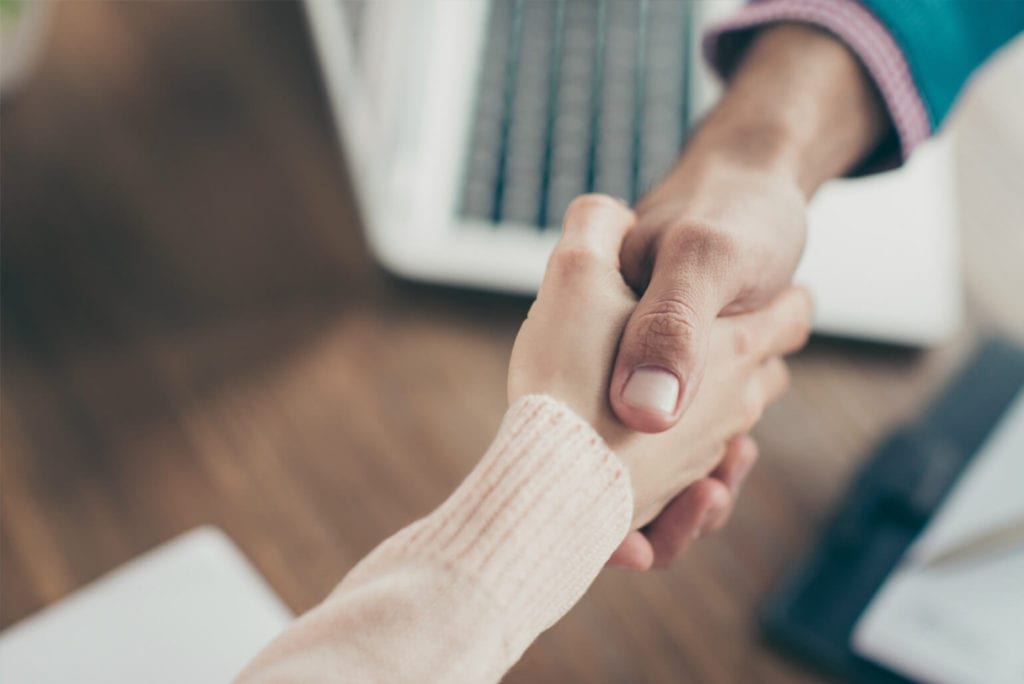 Close-up of two people shaking hands over a desk