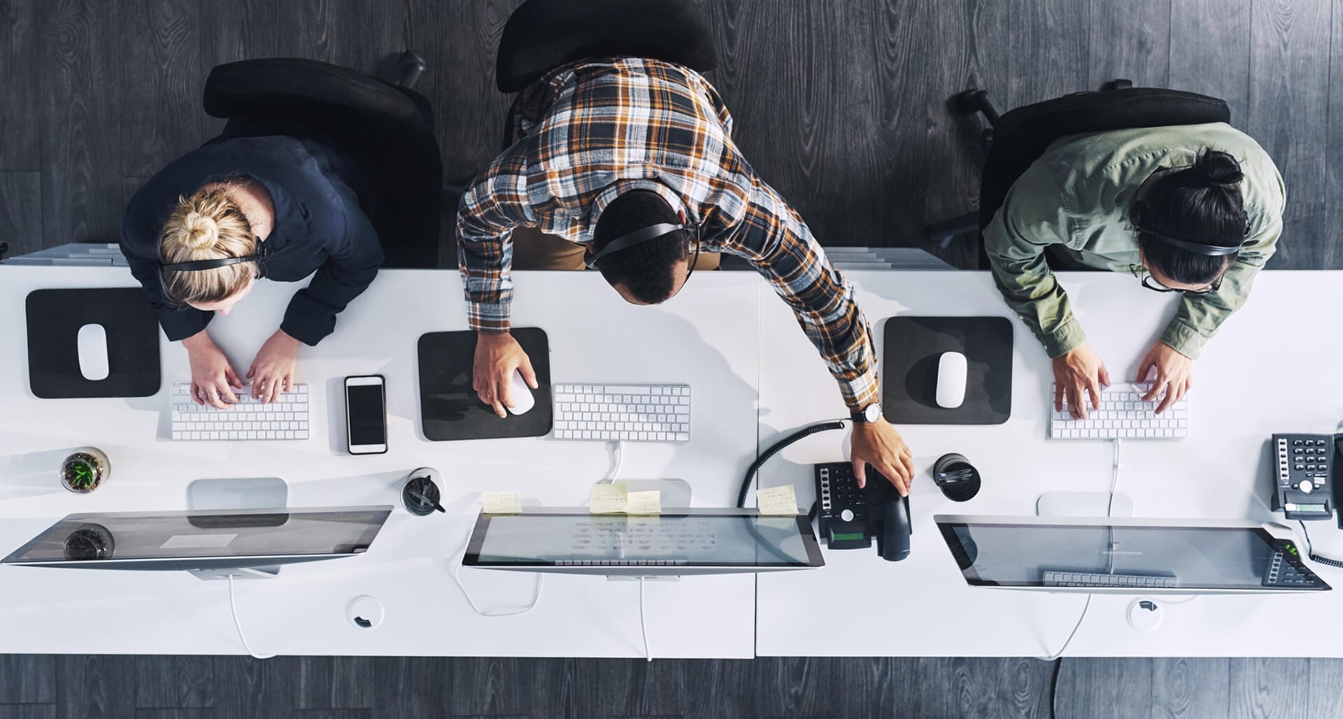 Aerial view of three employees working at computers with headsets