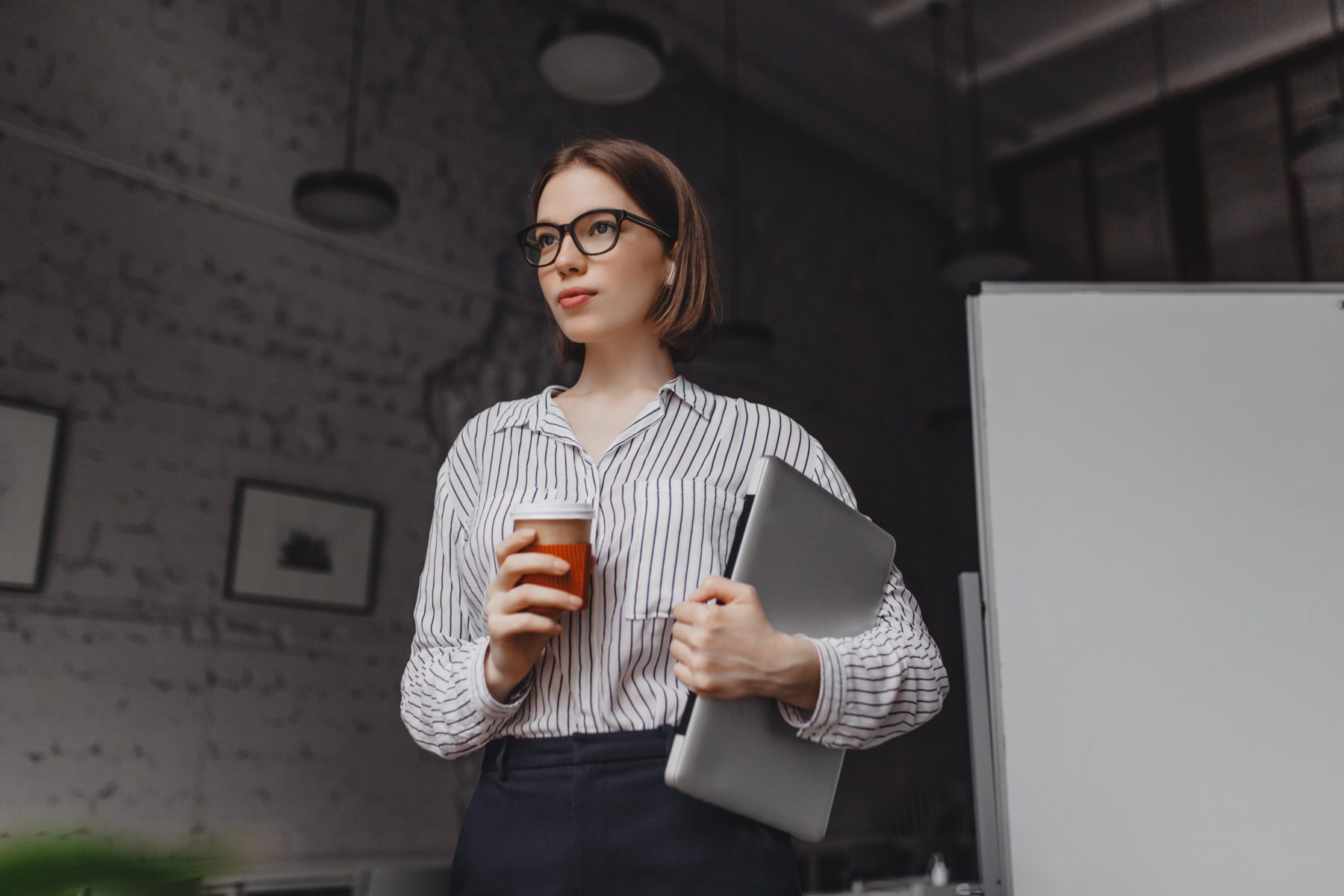 Portrait of intelligent woman in glasses holding cup of tea. Employee in stylish outfit posing with