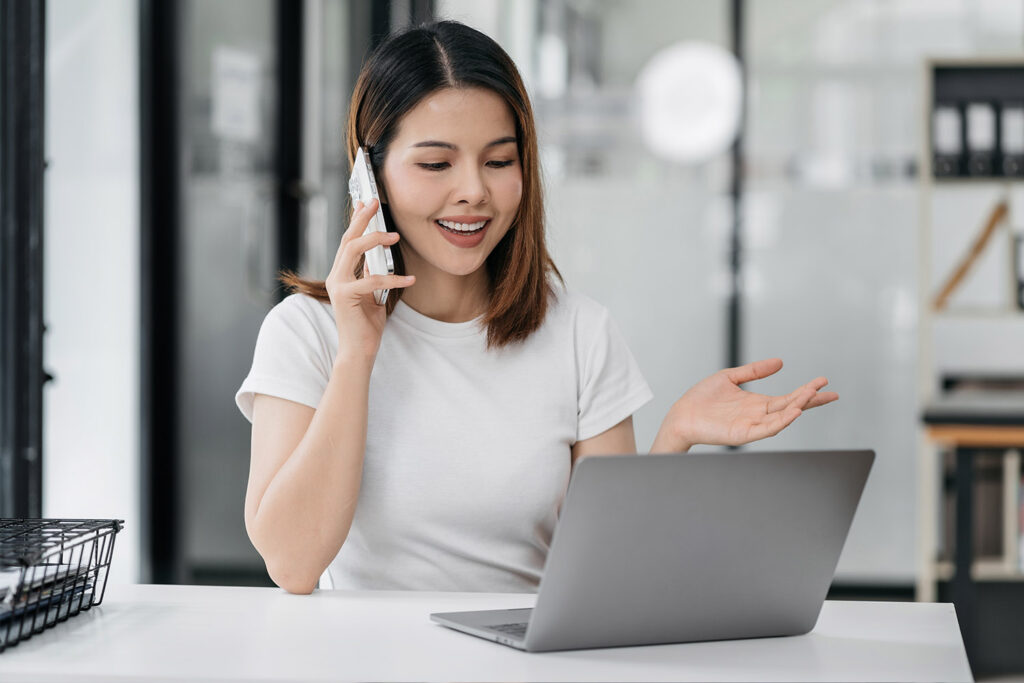 woman-at-desk-in-front-of-laptop-smiling-on-phone